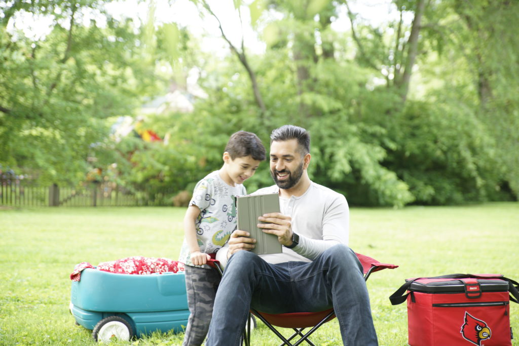 Online program student showing son coursework smiles on their faces outside together