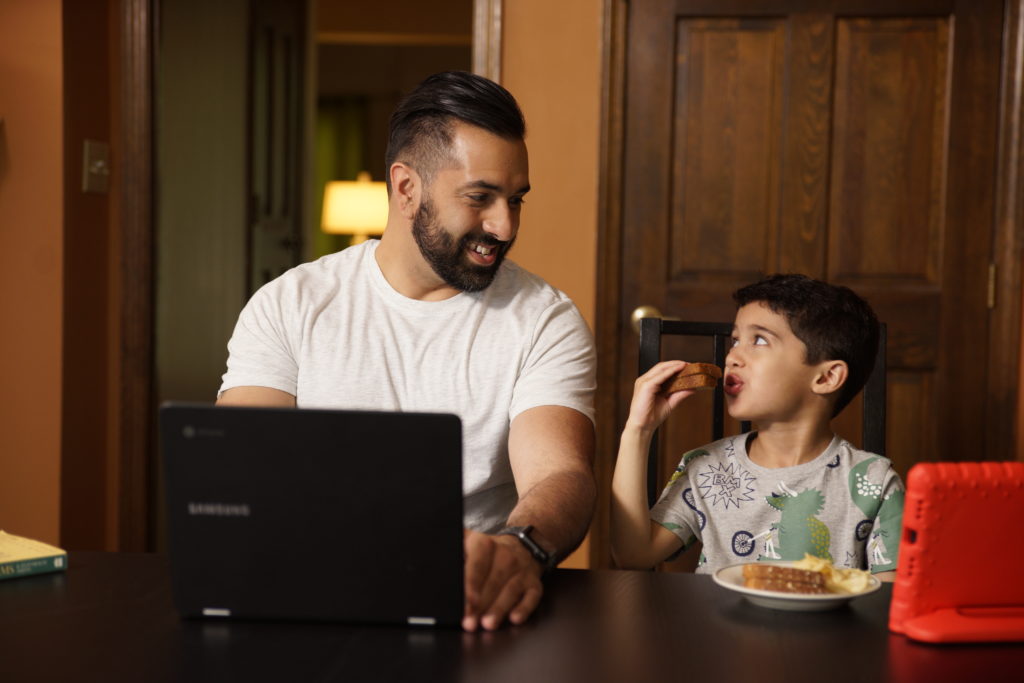 UofL online student having lunch with child while working on computer at home