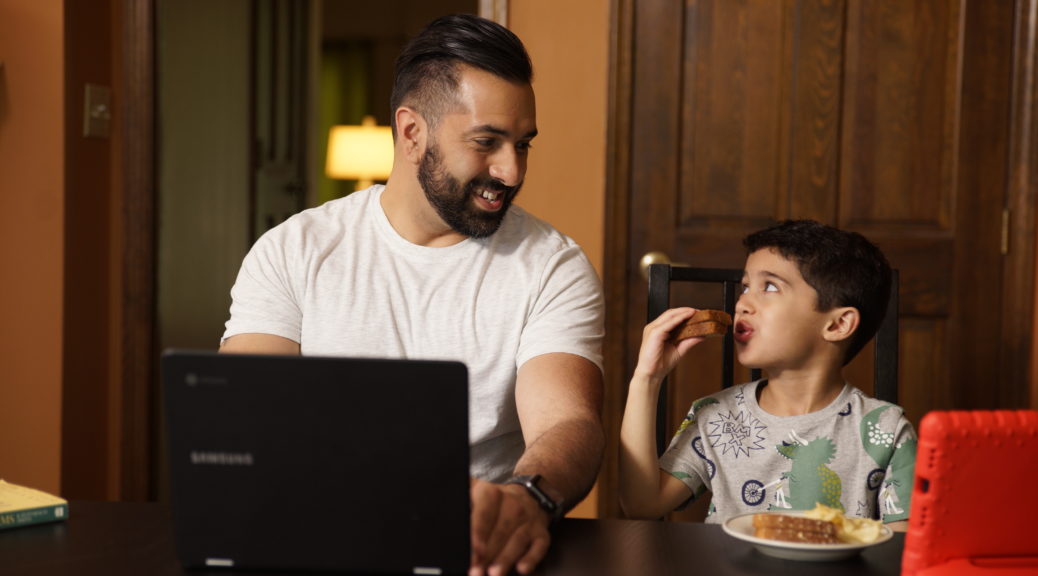 UofL online student having lunch with child while working on computer at home