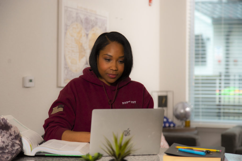 Military woman working at home on computer in military hoodie