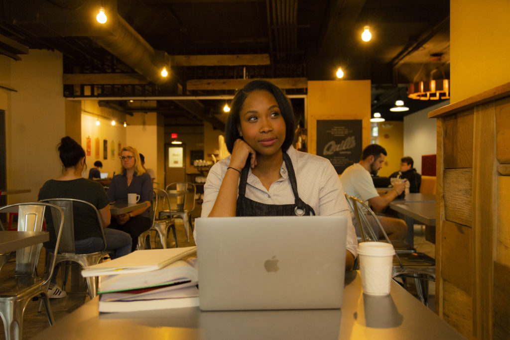 military woman working in coffee shop on laptop thinking about online program coursework